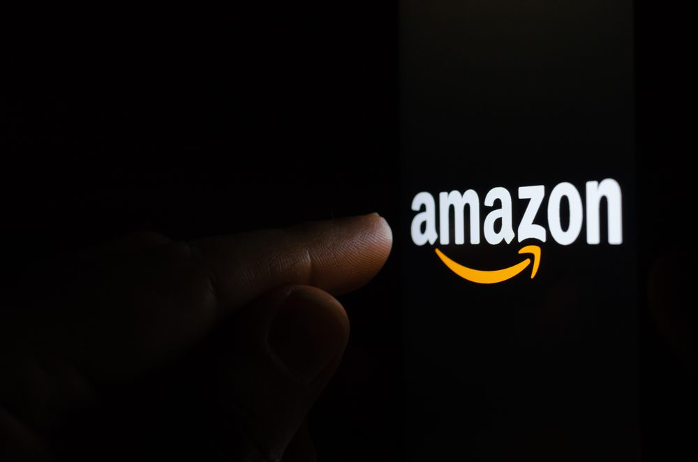 Logo Amazonu na obrazovce ve tmě a prst ukazující na něj.