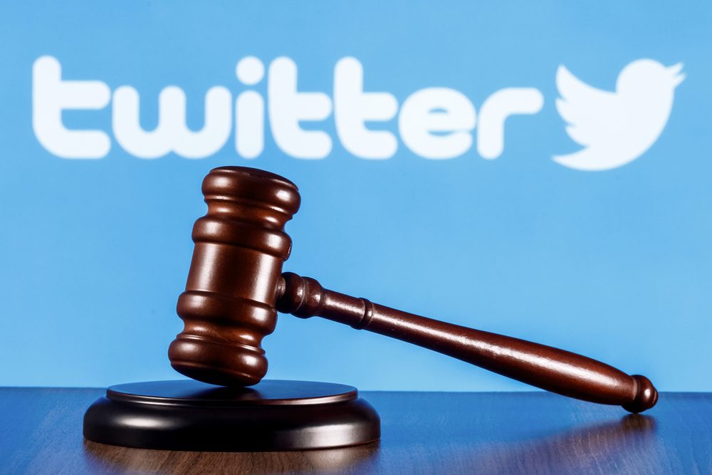Soudní kladívko na stole a na pozadí logo sociální sítě Twitter. Koncept soudního procesu.