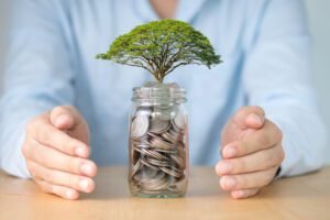 Podnikatel svýma rukama chrání strom, který roste na mincích ve sklenici. Koncept spoření a ochrany investic.